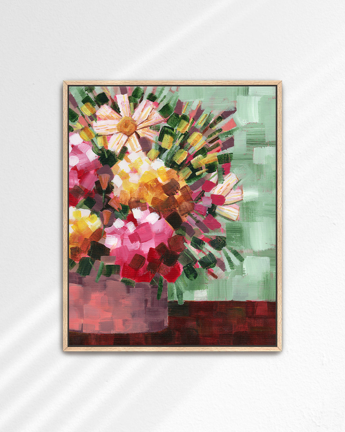A framed abstract floral art print by Jen Momtgomery featuring pink, yellow, red, and white flowers with green and brown accents, displayed on a light gray wall with soft diagonal shadows.
