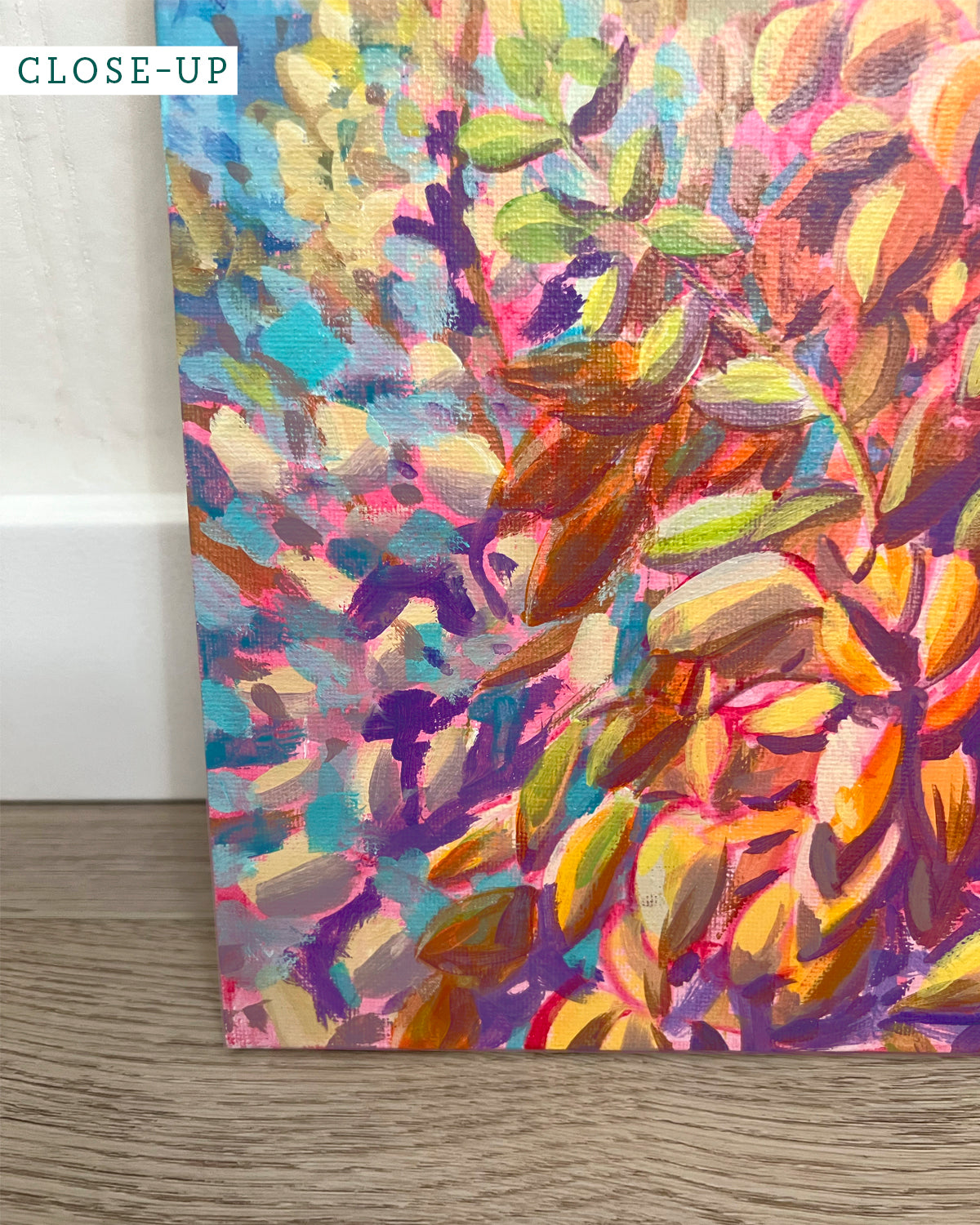 Close-up of an acrylic painting by Jen Montgomery showing a yucca plant with yellow, green, and orange brushstrokes against a textured blue and purple background, mounted on a white wall.