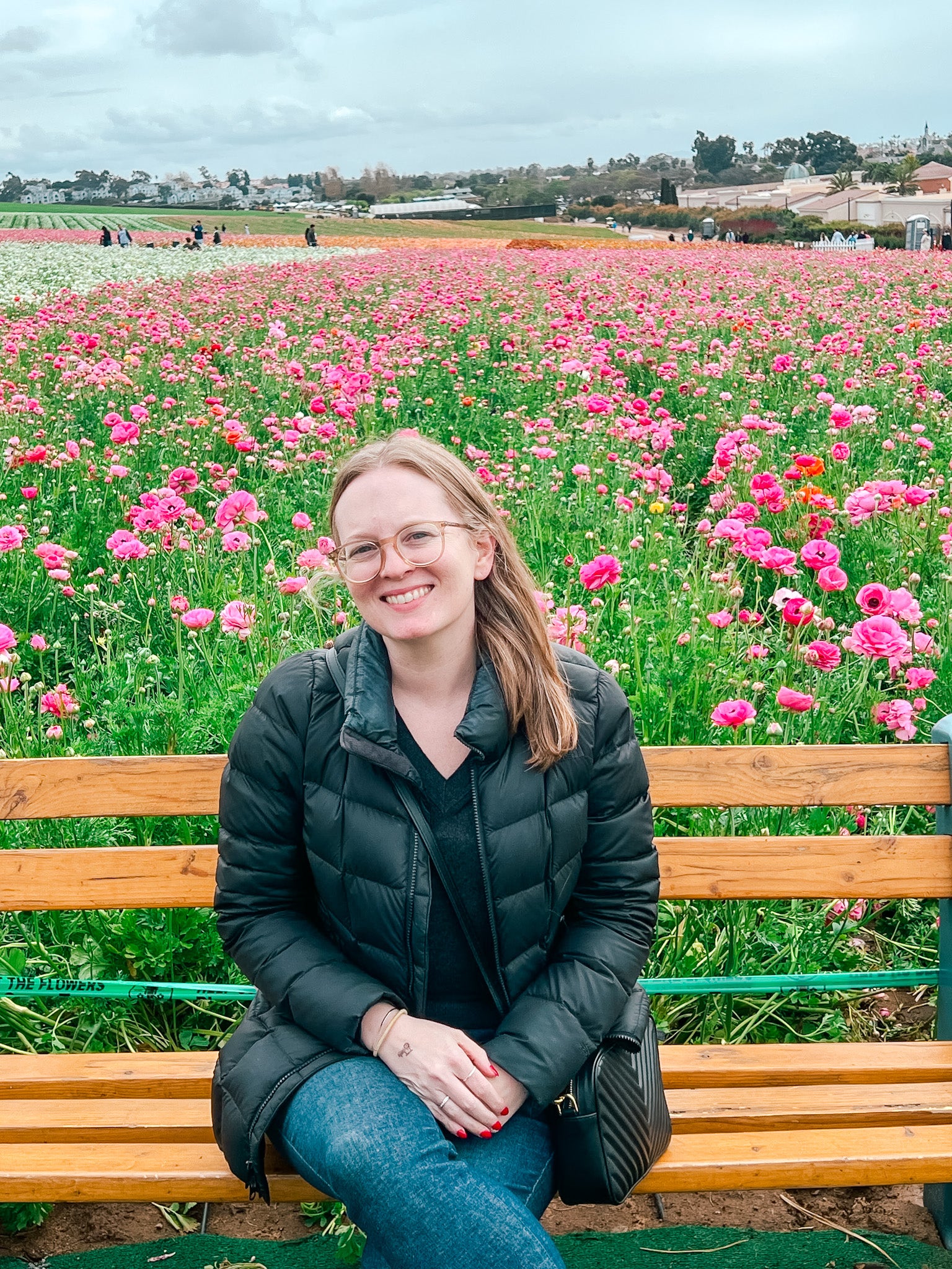 Jen Montgomery sitting on a bench in a field of pink flowers with a scenic background.