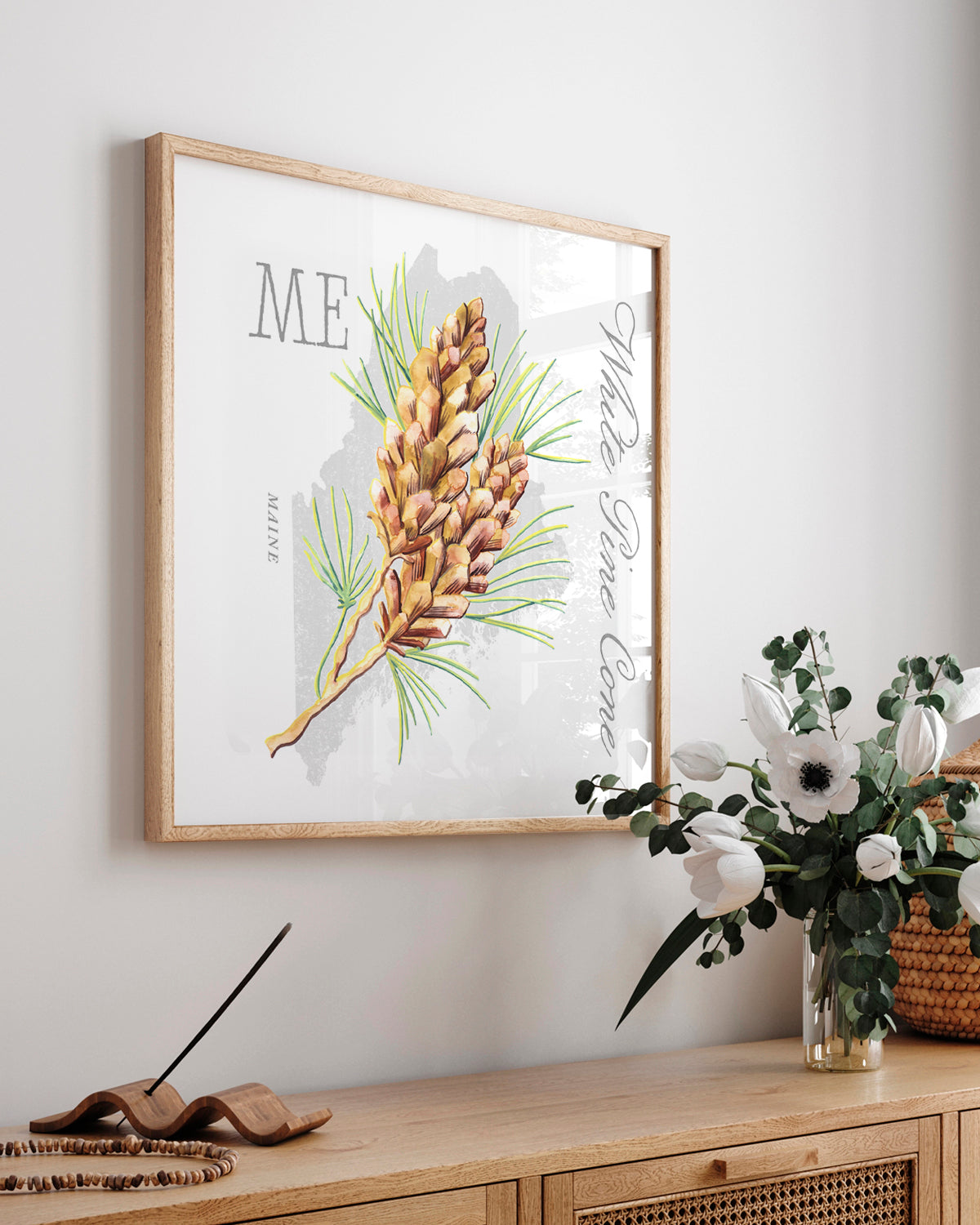 Framed Maine state flower botanical wall art by Jen Montgomery hanging on a light gray wall above a wooden console table. 