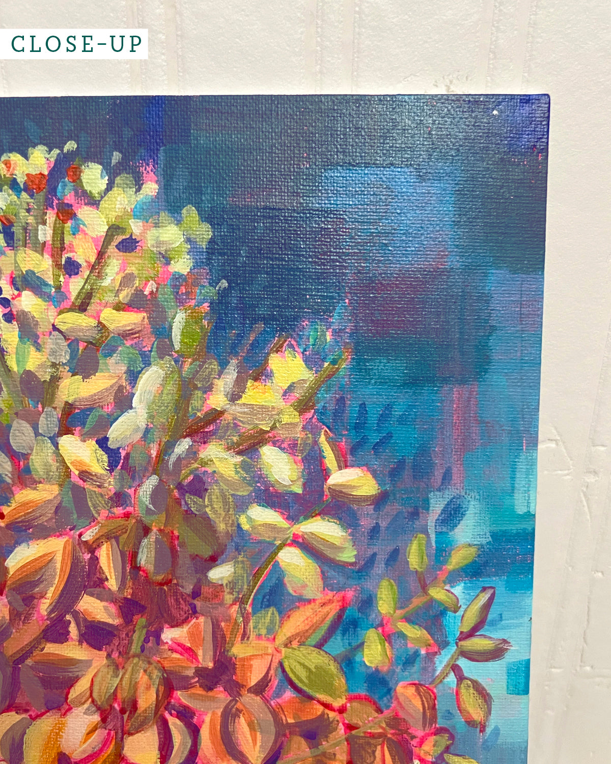 Close-up of an acrylic painting by Jen Montgomery showing a yucca plant with yellow, green, and orange brushstrokes against a textured blue and purple background, mounted on a white wall.