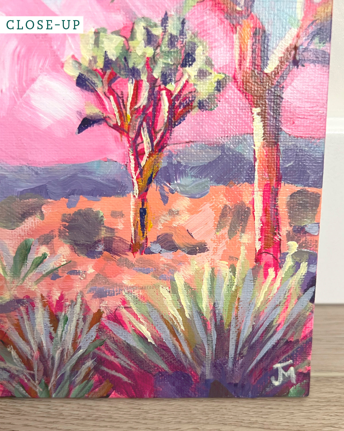 A close-up of a colorful painted desert landscape by Jen Montgomery on a textured canvas, featuring pink sky, two trees, and spiky desert plants. A small 'CLOSE-UP' label appears in the top-left corner.